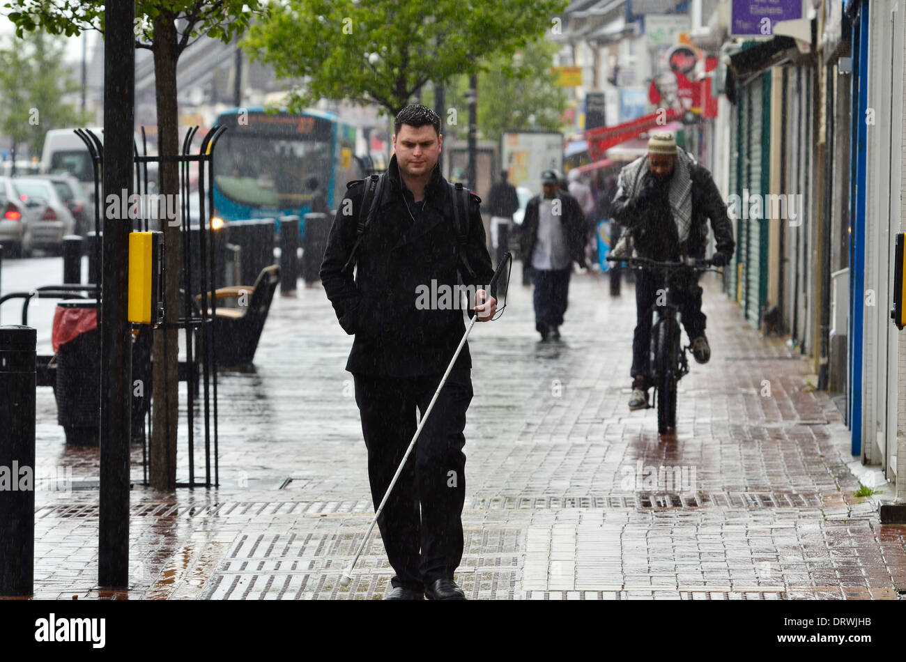 Blind man with white stick walking on wet pavement during rain shower in Luton Stock Photo