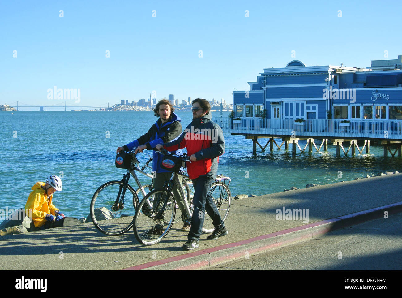 friends walk their rental bikes on Sausalito sidewalk along the Bay Stock Photo