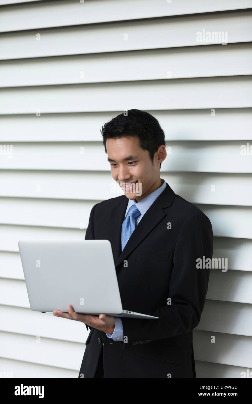 Chinese business Man using his laptop out doors in modern city. Business on the go concept. Stock Photo