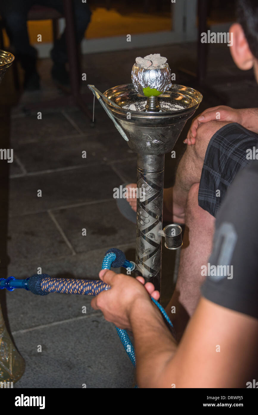 smoking a shiska young man sits with and smokes a waterpipe on a hot evening at a lebonese restaraunt not see his face. Stock Photo