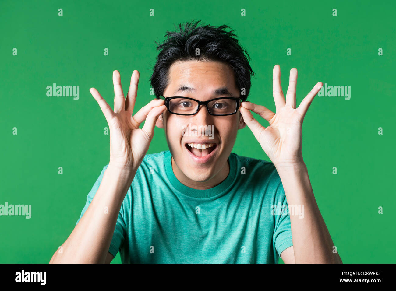 Surprised and amazed looking Asian man standing against green background. Stock Photo