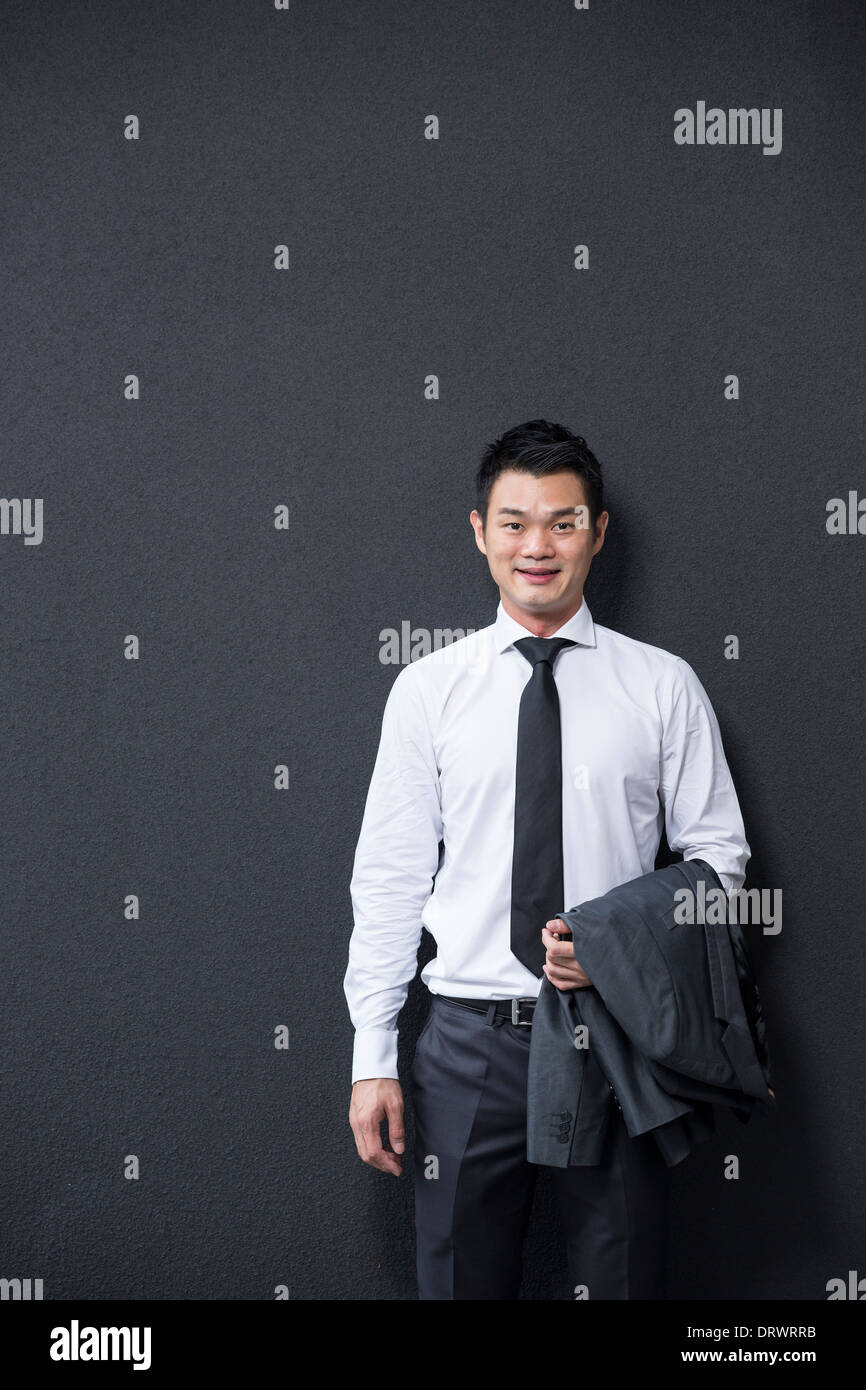 Chinese Business man leaning on a black wall. Handsome young Chinese business man leaning against a black wall. Stock Photo