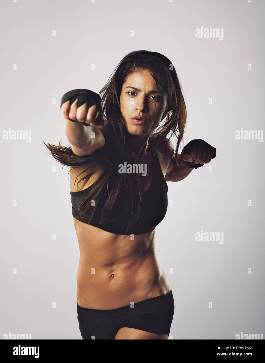 Young muscular woman practicing boxing. Middle eastern female throwing punch towards camera against grey background Stock Photo