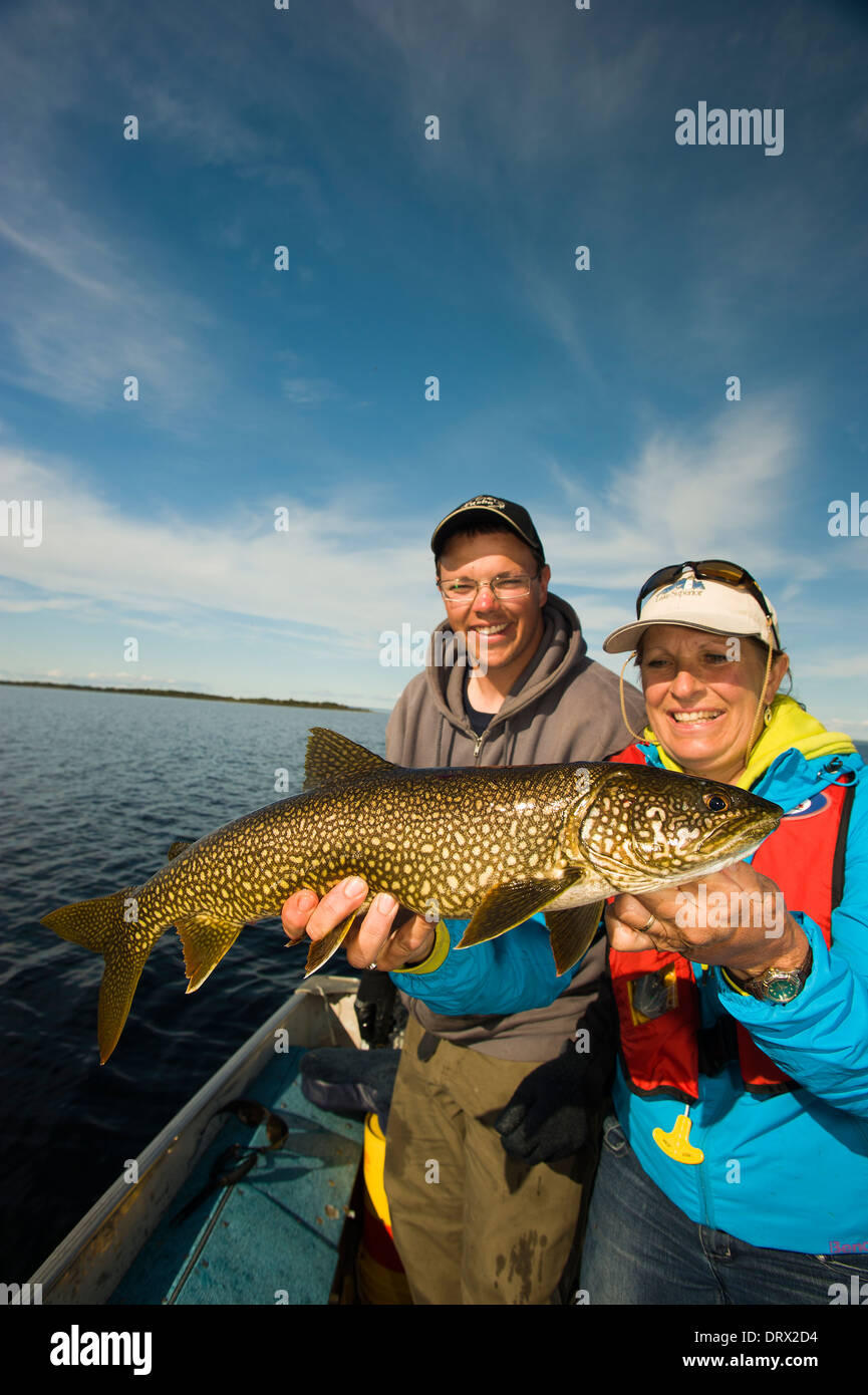 Woman angler holds up a large summer lake trout with a young man looking on. Stock Photo