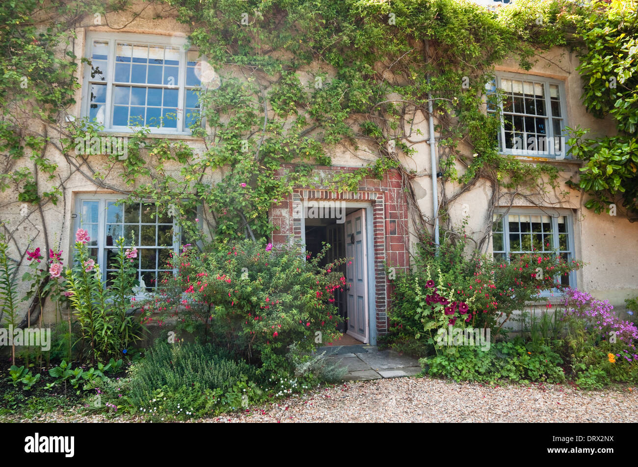Charleston Farmhouse, Sussex, showing front elevation surrounded by informal border planting and wall climbing roses / shrubs. Stock Photo