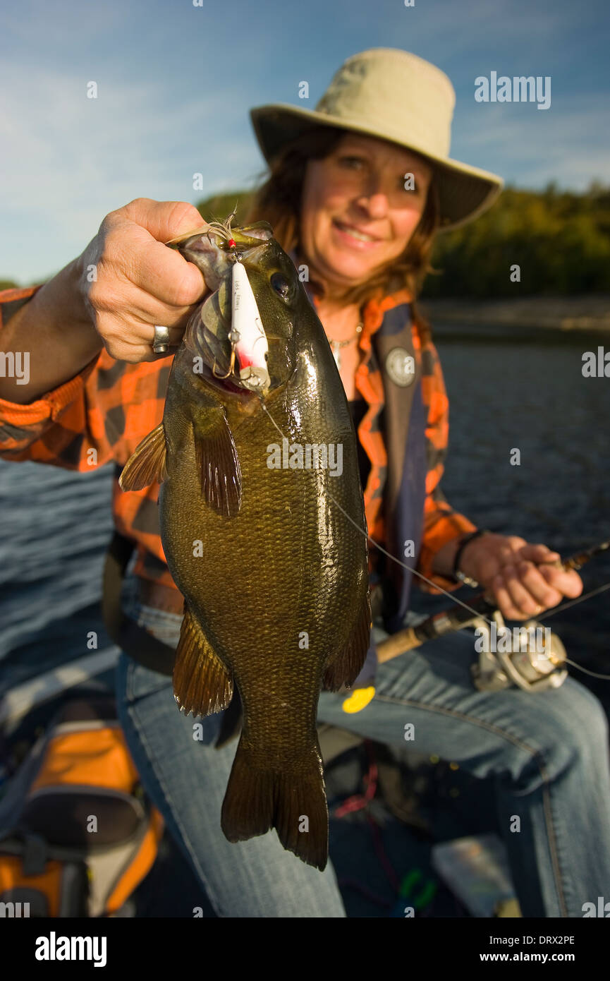 Woman angler holding the smallmouth bass she caught in a boat on a lake in Northern Ontario. Stock Photo