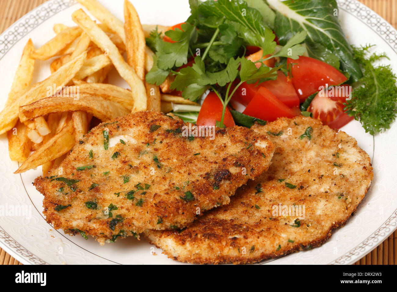 breaded homemade chicken schnitzels or escalopes with french fries and a tomato and green salad
