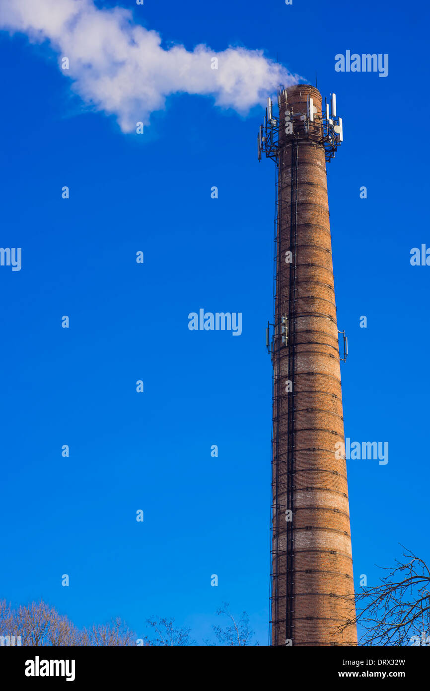 Smoking brick tower with mobile antenna on top against blue sky Stock Photo
