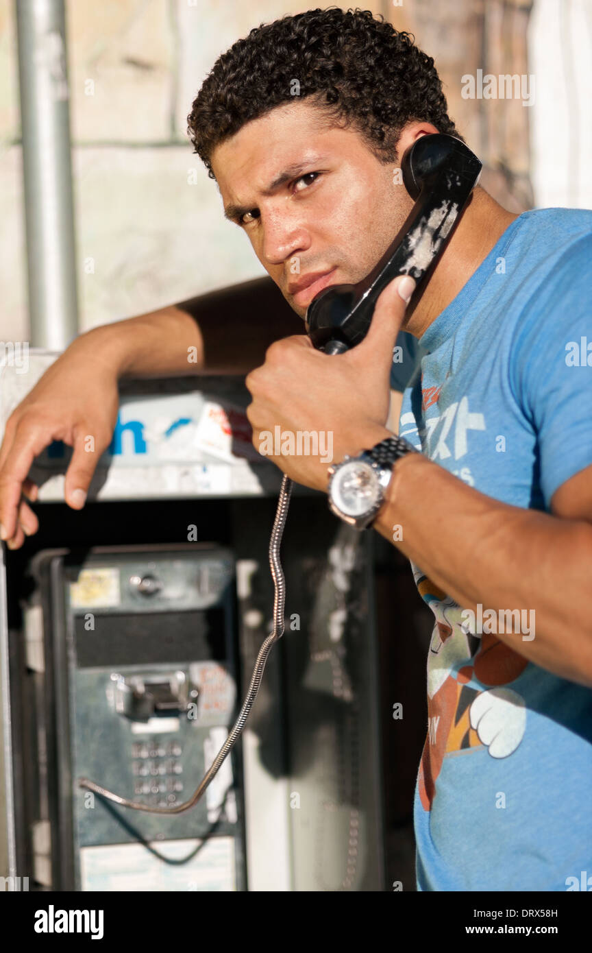 A black man making a phone call on an American public telephone. He looks a bit rebellious and curious. Stock Photo