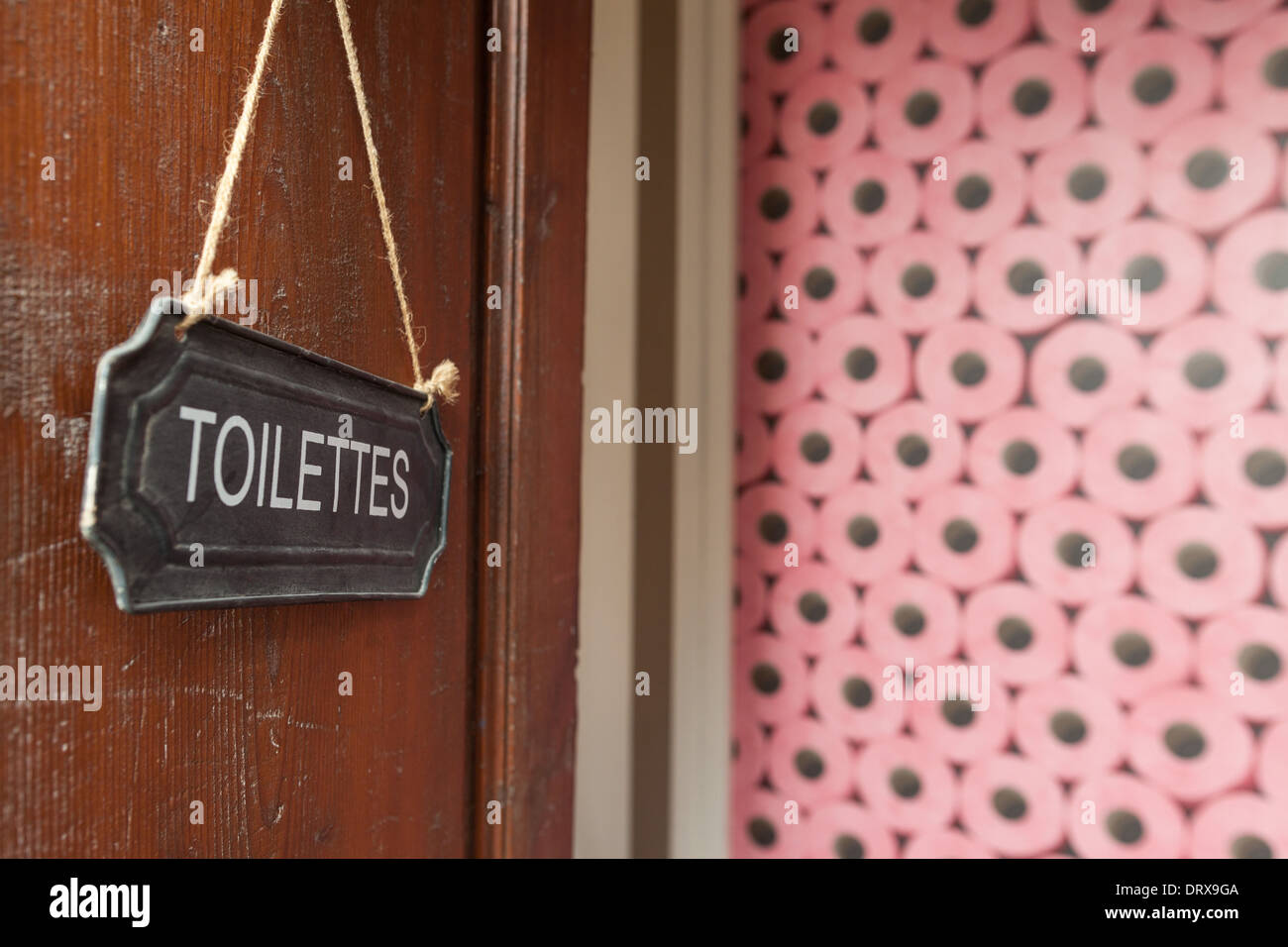 Toilet sign hanging on a wooden doors with stack of pink toilet paper
