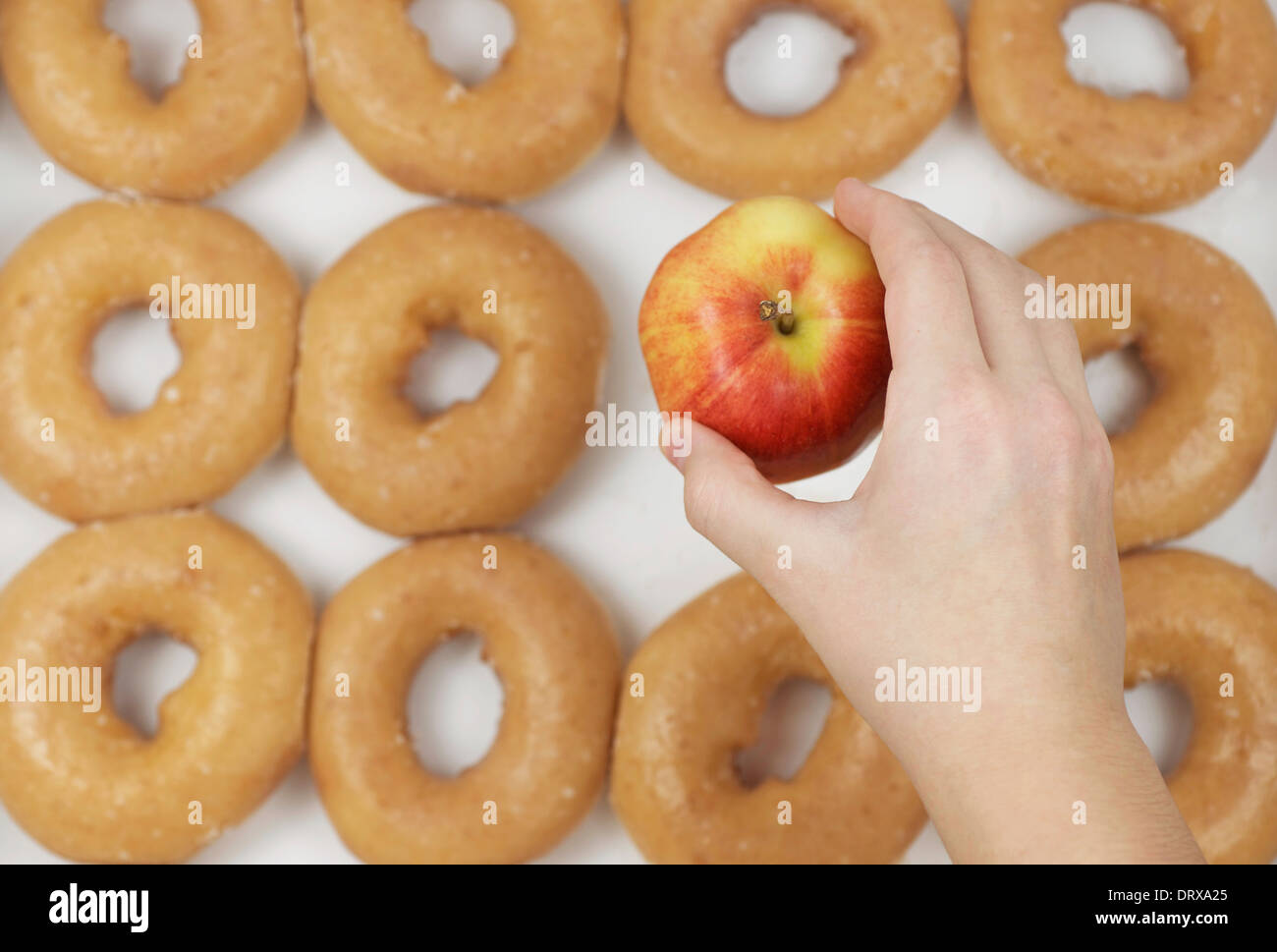 A dozen glazed donuts with an apple that is being picked or chosen by a right hand. Stock Photo