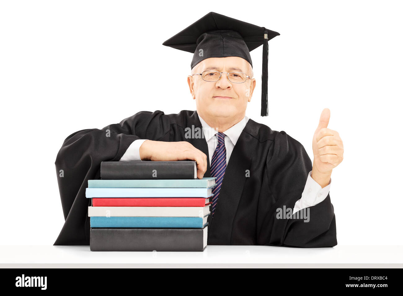 Middle aged college professor seated on table with stack of books and giving thumb up Stock Photo