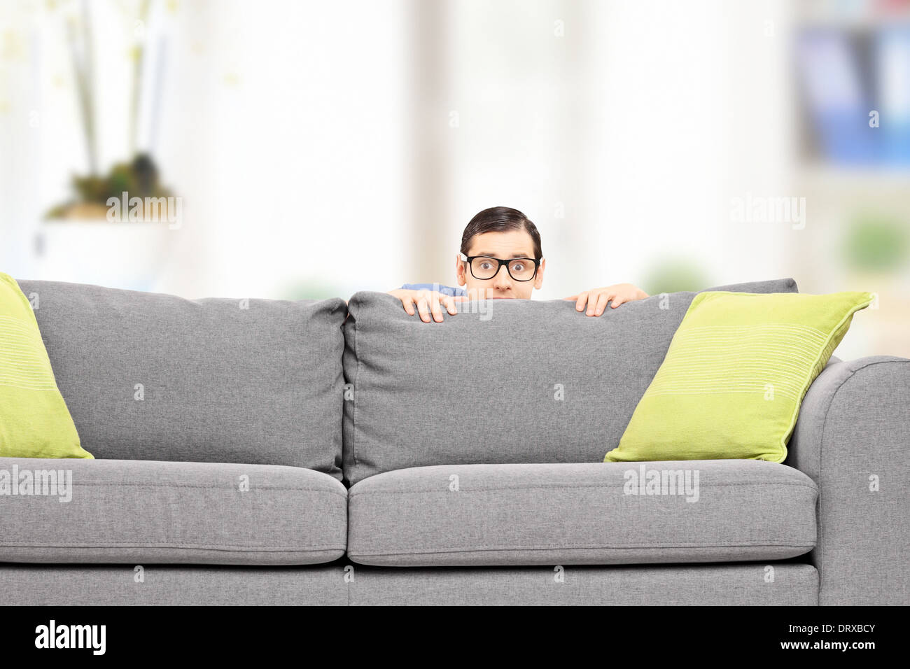 Frightened man hiding behind a sofa at home Stock Photo