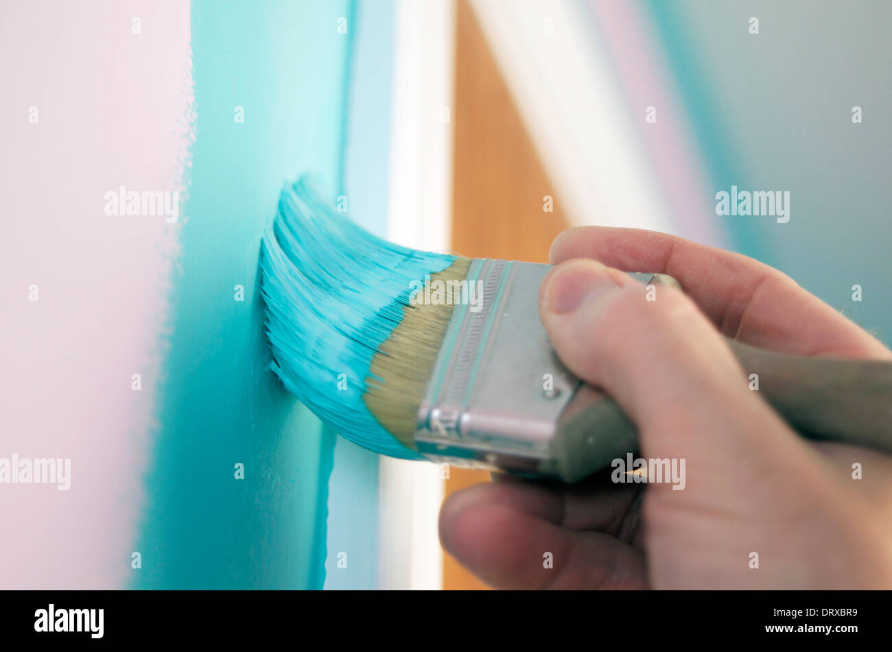 Hand holding paintbrush with turquoise paint painting a wall. Stock Photo