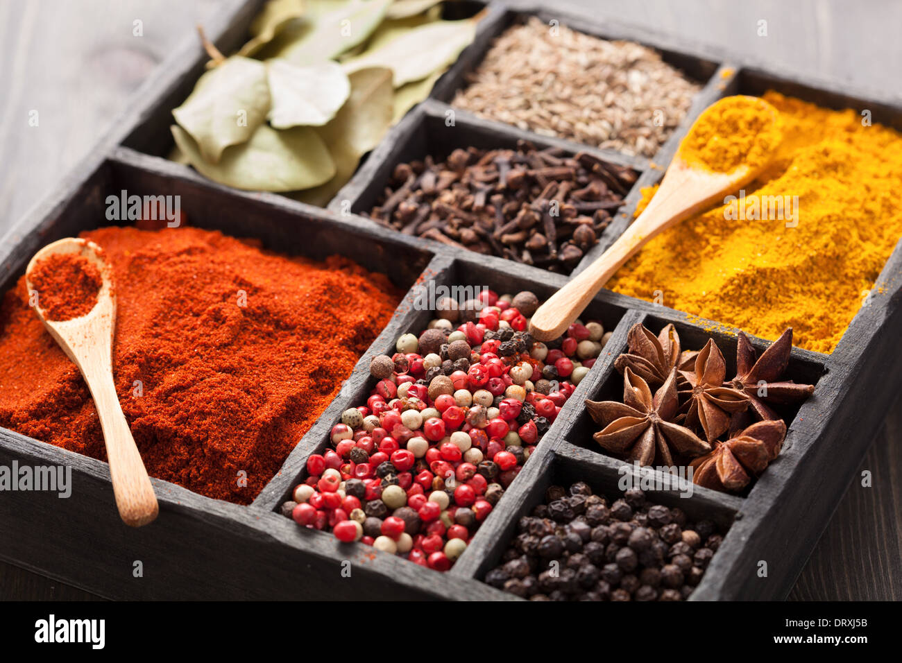 spices in box: pink and black pepper, paprika powder, curry, bay leaf; anise; clove; cumin Stock Photo