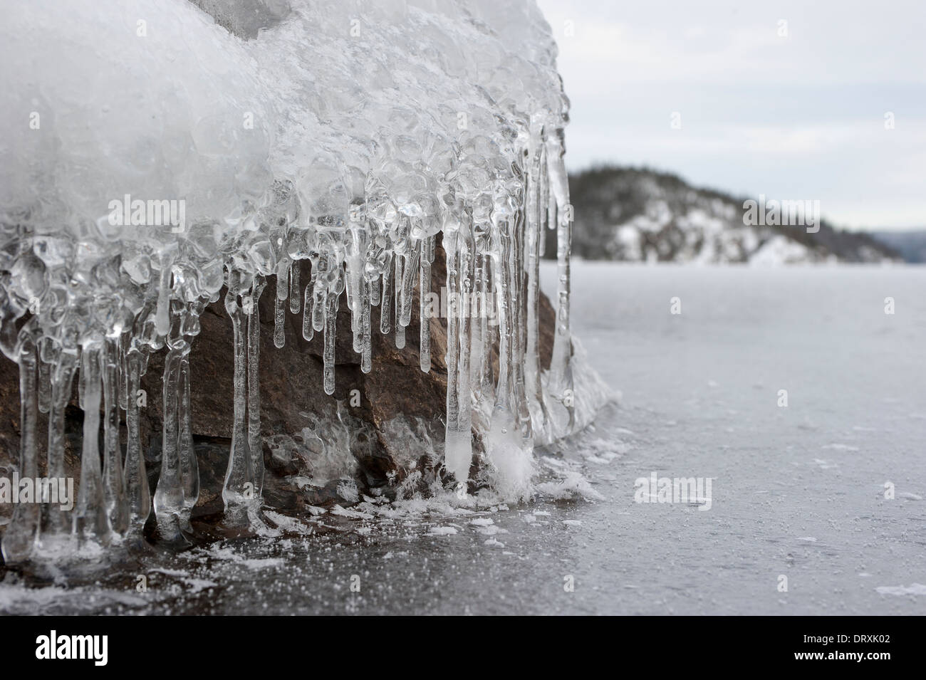 Ice melting off a rock at a lakeshore in winter. Stock Photo