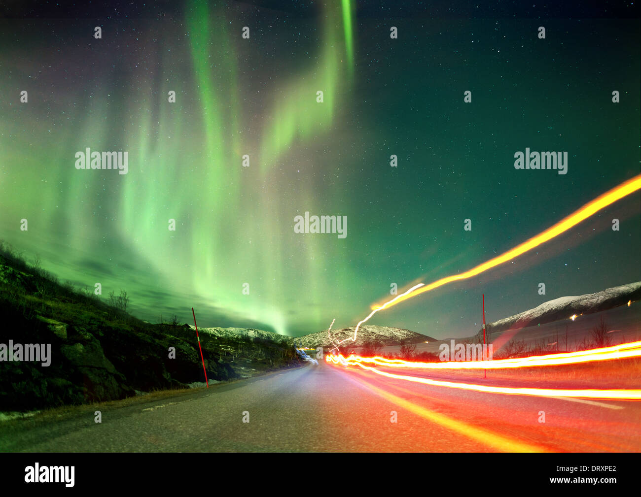 The Northern Lights in Norway landscape with red light trails on a road. Stock Photo
