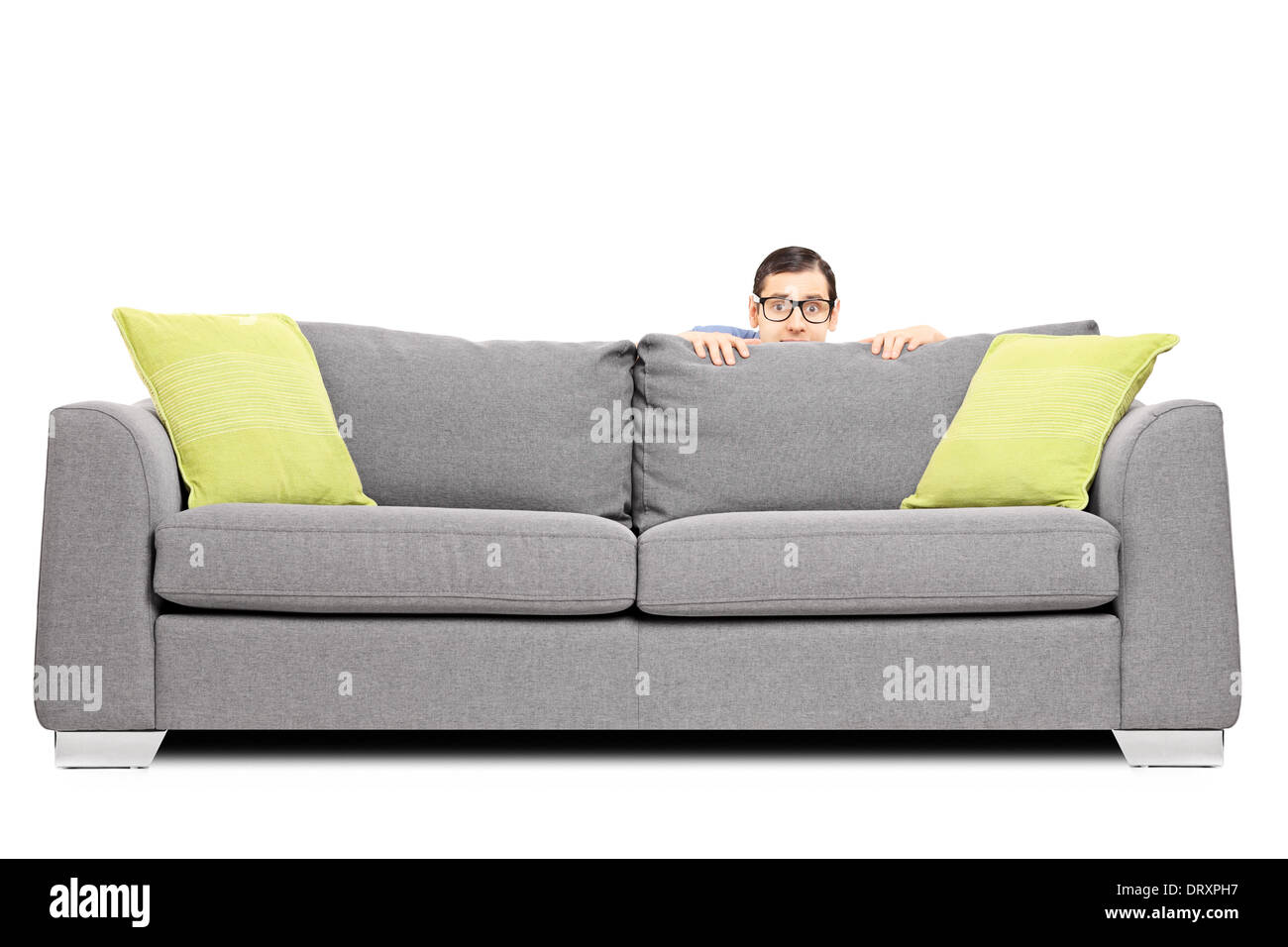 Frightened man hiding behind a sofa isolated on white background Stock Photo