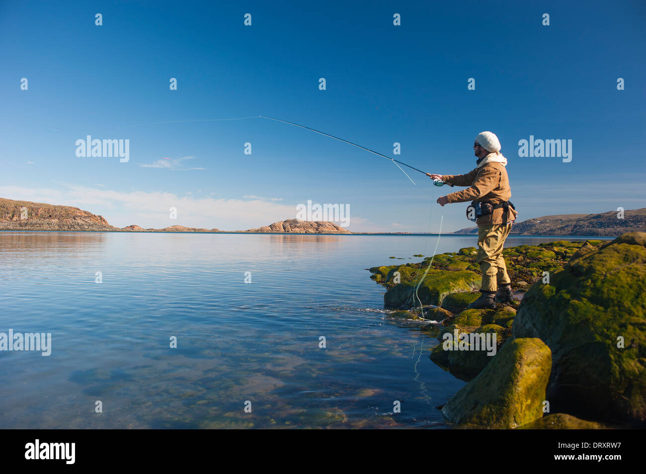 Angler casts off the rocky arctic shore in northern Canada. Stock Photo