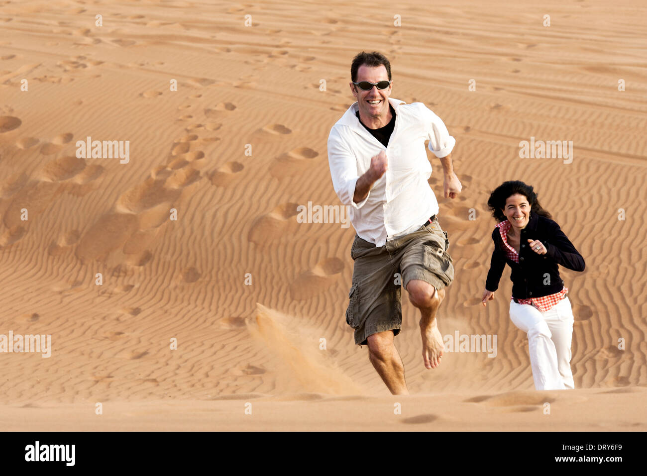 Couple running up desert dune Stock Photo