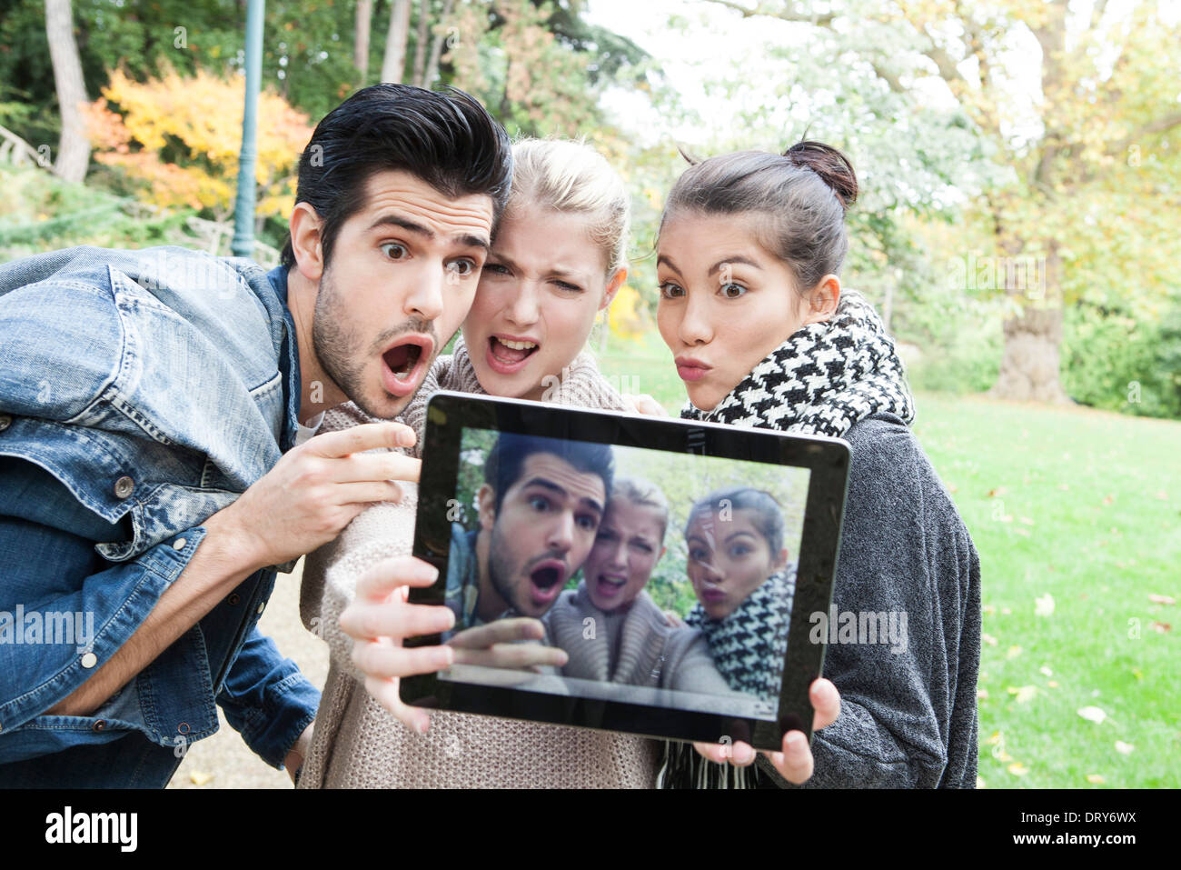 Friends photographing themselves making funny faces with digital tablet outdoors Stock Photo