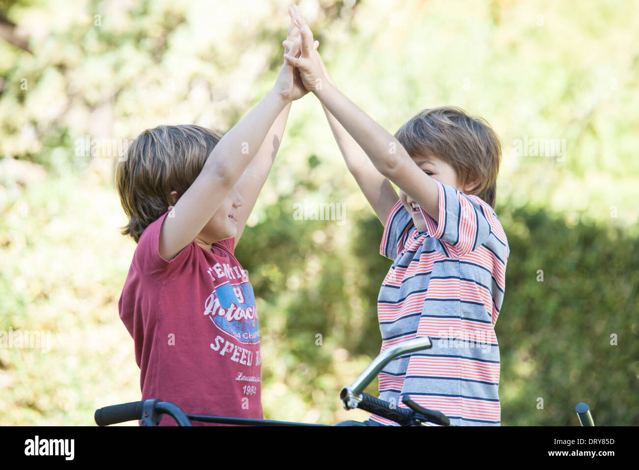 Boys on bicycles giving high fives Stock Photo