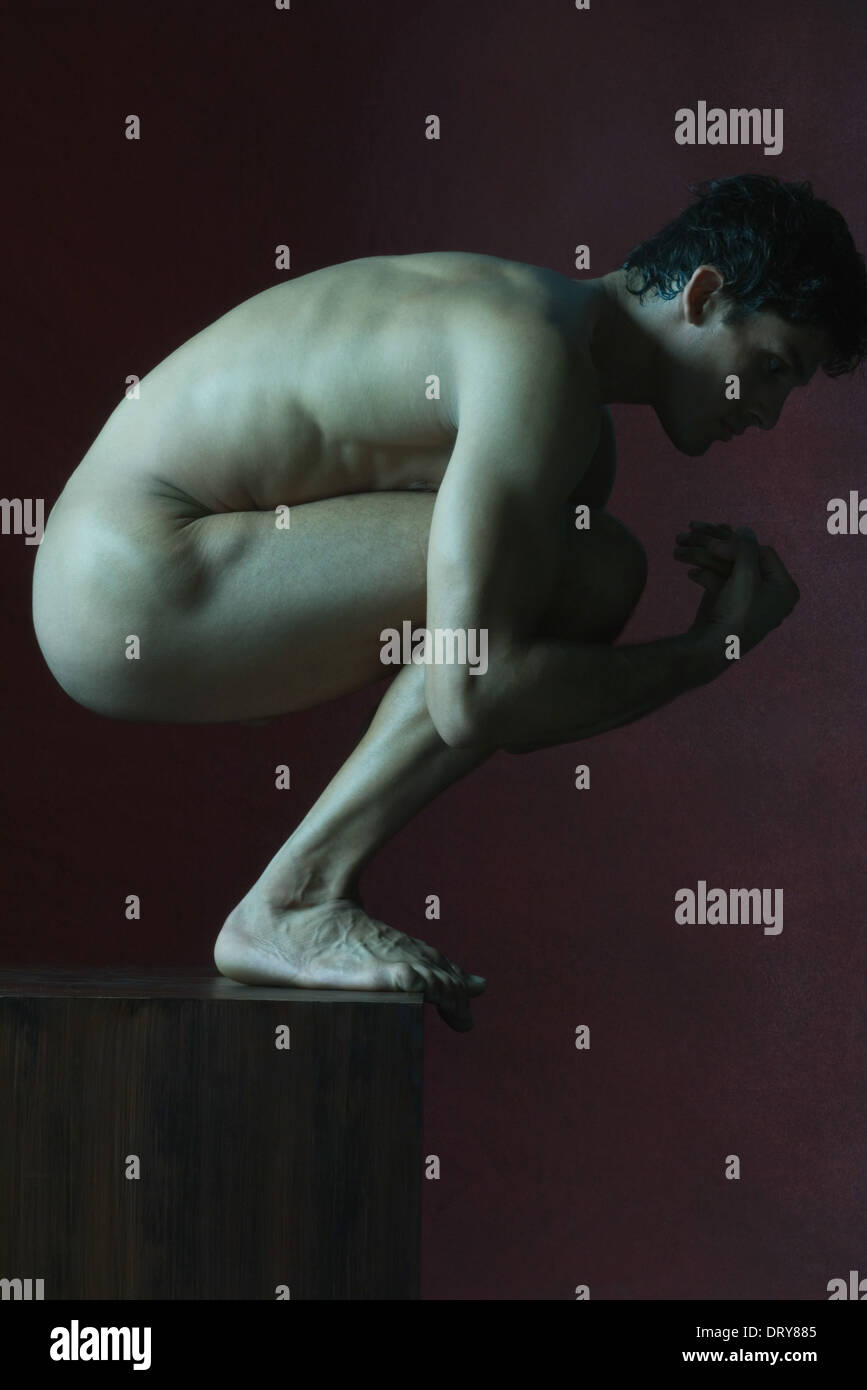 Nude man crouching, side view Stock Photo
