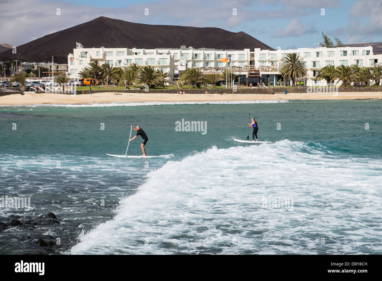 Two men on surf boards paddleboarding on big waves in sea off Playa Charcos beach in Costa Teguise, Lanzarote, Canary Islands Stock Photo