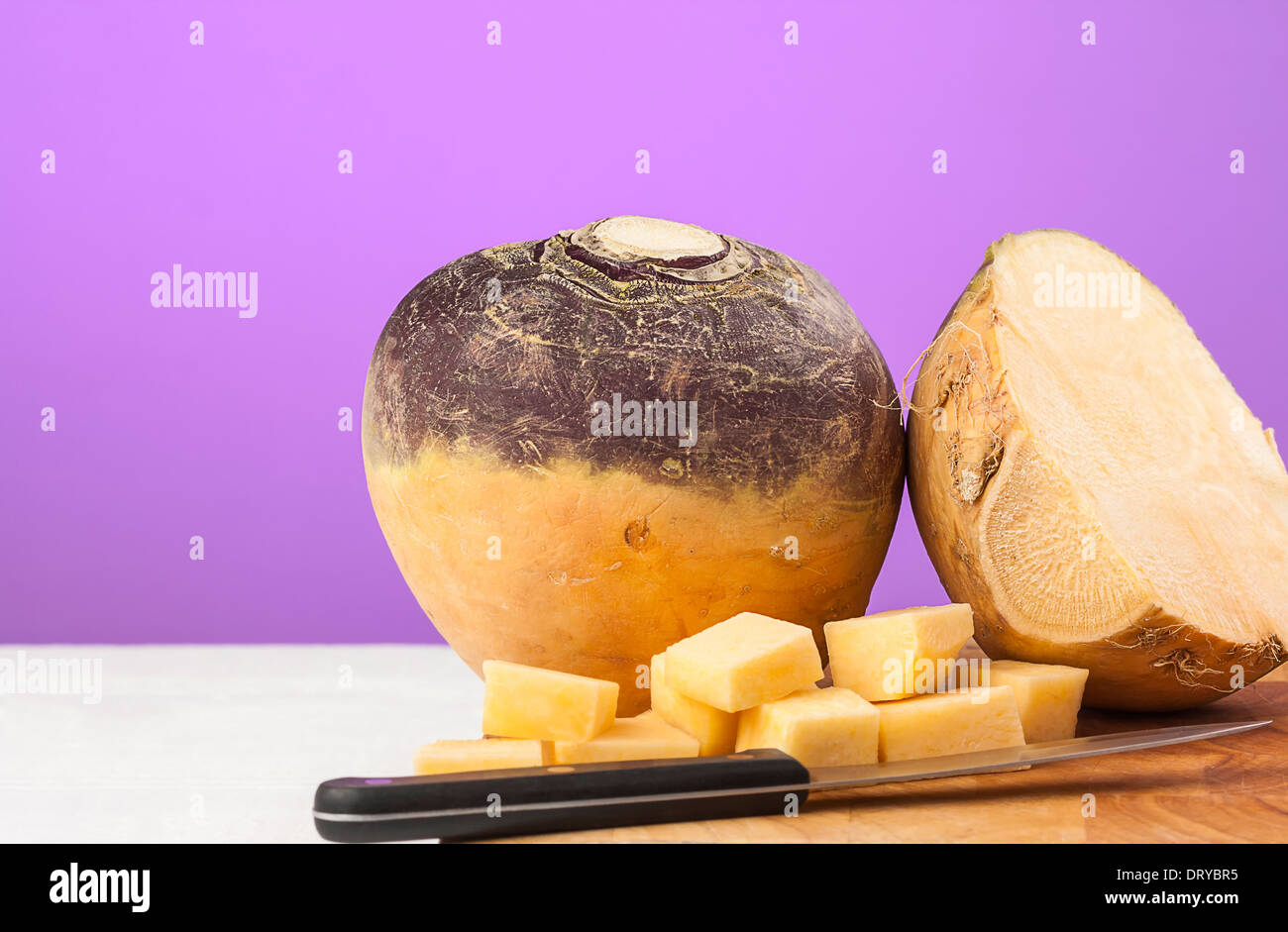 Swede root vegetables with chopped small chunks and kitchen knife on chopping board. Stock Photo