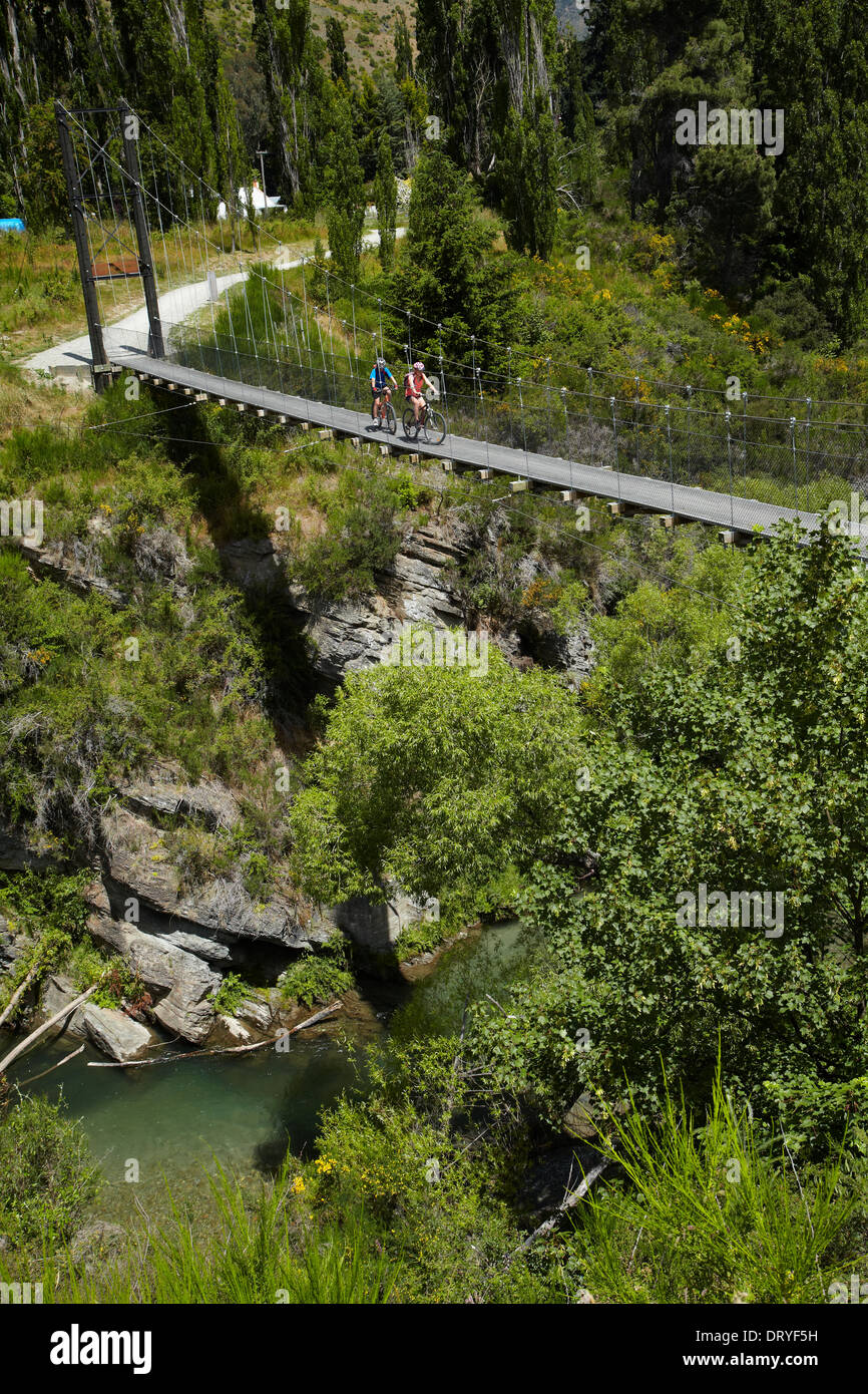 Mountain bikers crossing suspension bridge on Arrow River Bridges Ride, near Arrowtown, Otago, South Island, New Zealand Stock Photo