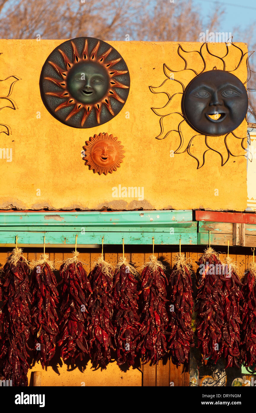 Dried peppers and art displayed against an adobe structure lit by late afternoon sun. Stock Photo