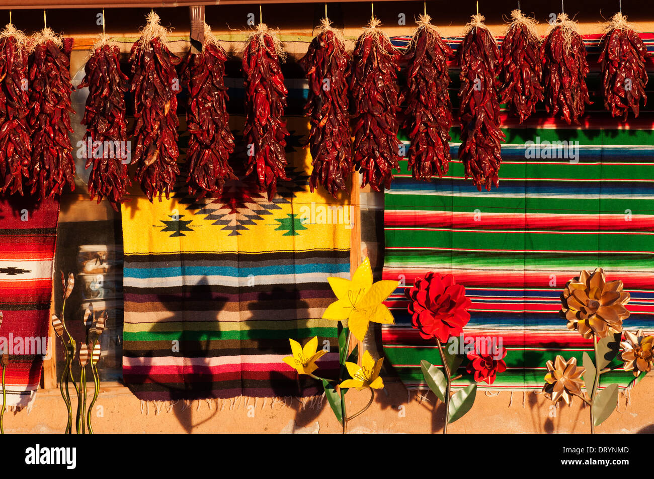 Dried peppers, rugs and art displayed against an adobe structure and ...