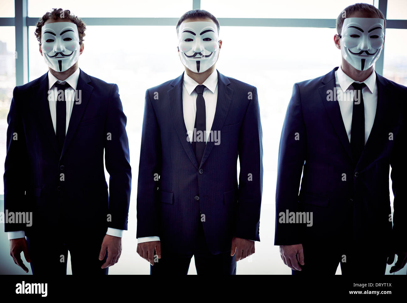 Portrait of three colleagues hiding behind Guy Fawkes masks Stock Photo