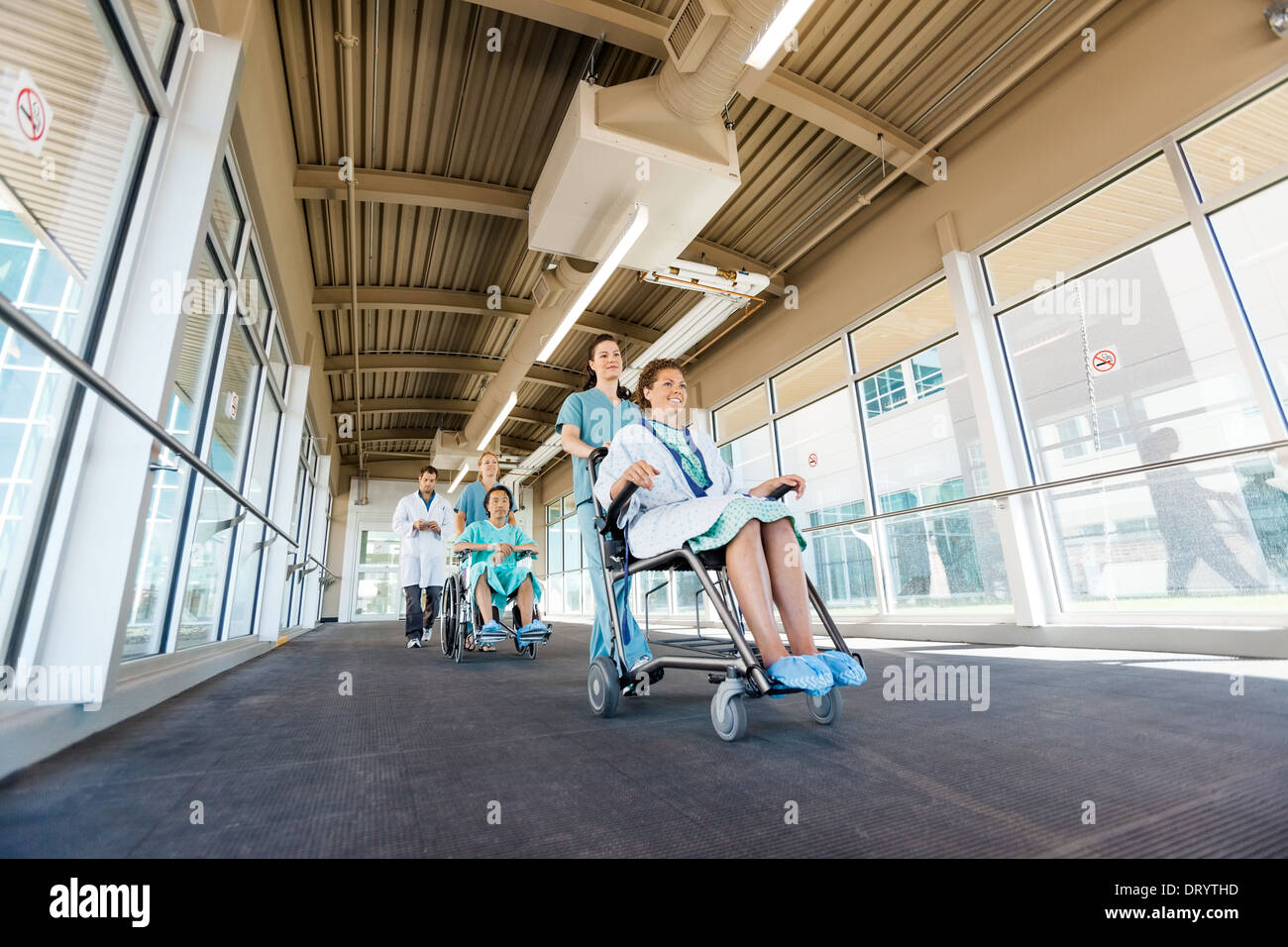 Nurses Pushing Patients On Wheelchairs At Hospital Corridor Stock Photo