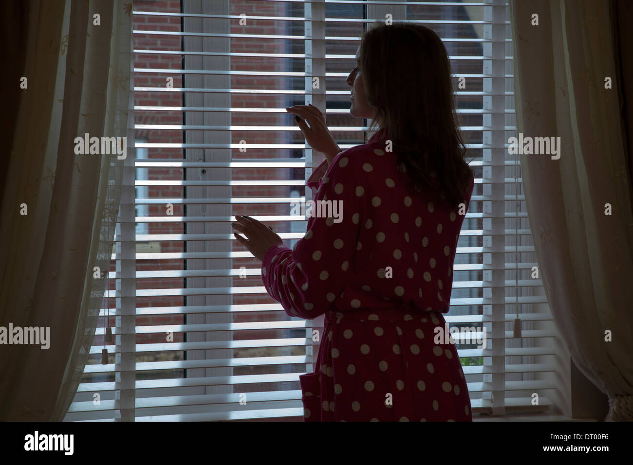 Beautiful woman in sheer nightgown looking out of a window with  backlighting Stock Photo - Alamy