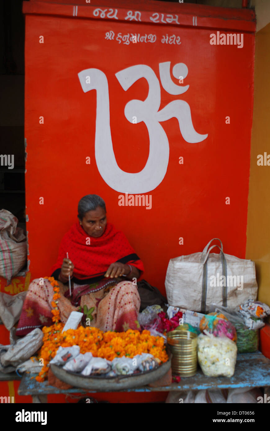 Hindu woman making a flower garland with marigolds. Above her, the hindu symbol Om ( India) Stock Photo