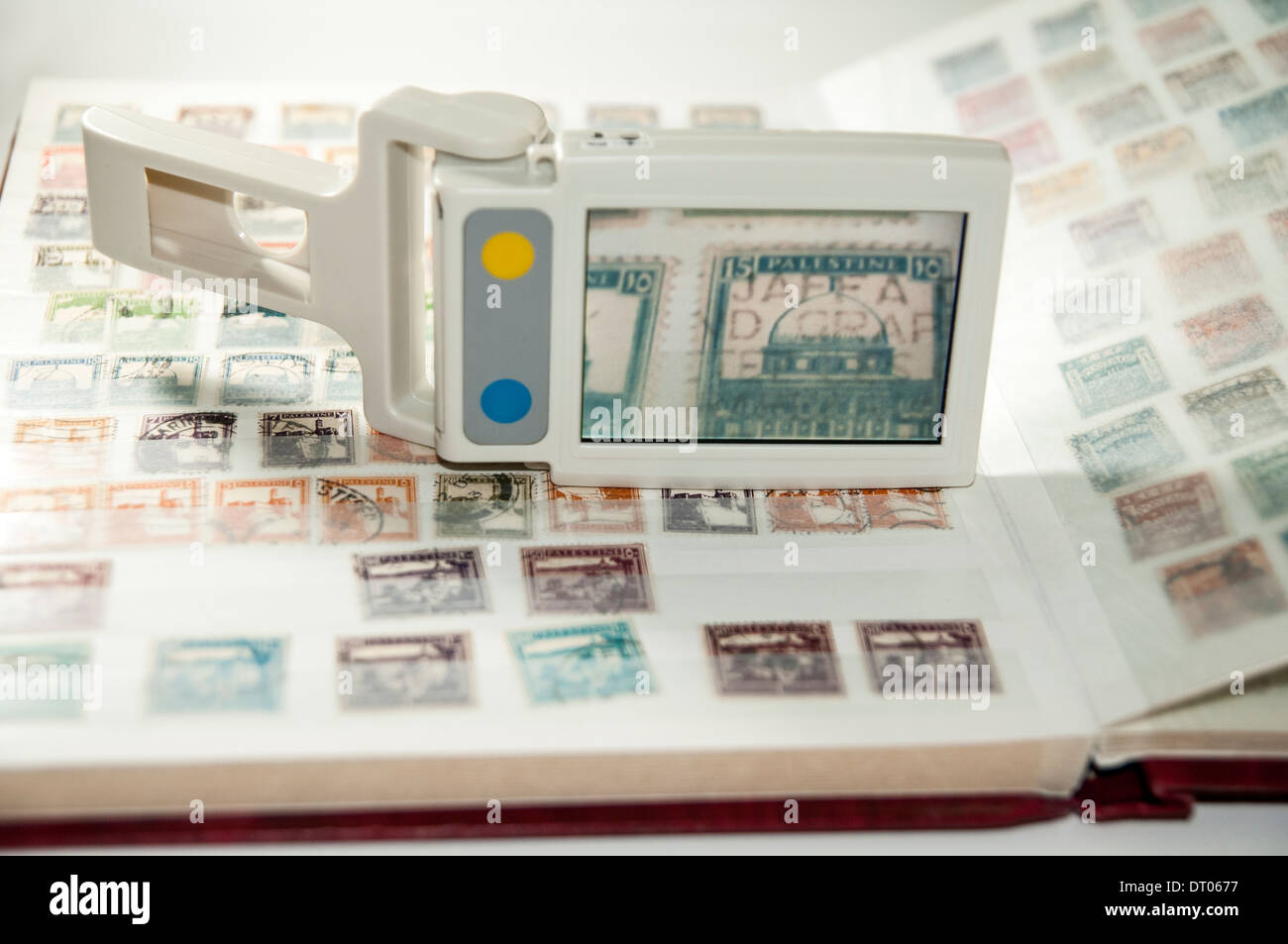 A vision impaired stamp collector uses a handheld electronic magnifier to inspect a stamp Stock Photo