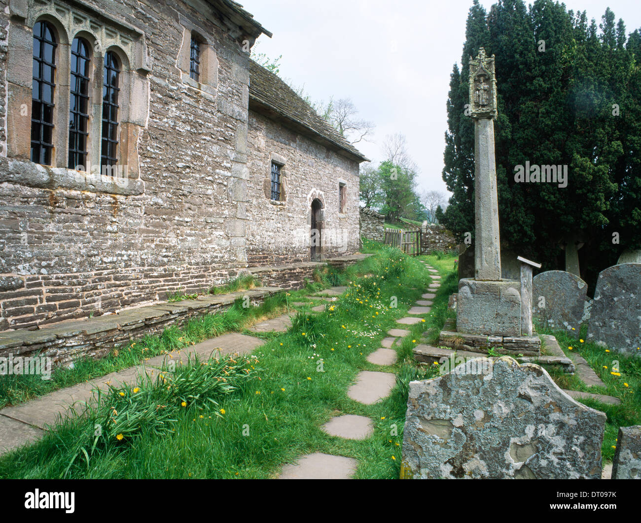 St Issui's church, Partrishow, Powys: churchyard preaching cross opposite stone benches running alongside chancel & nave. Paved Public footpath. Stock Photo