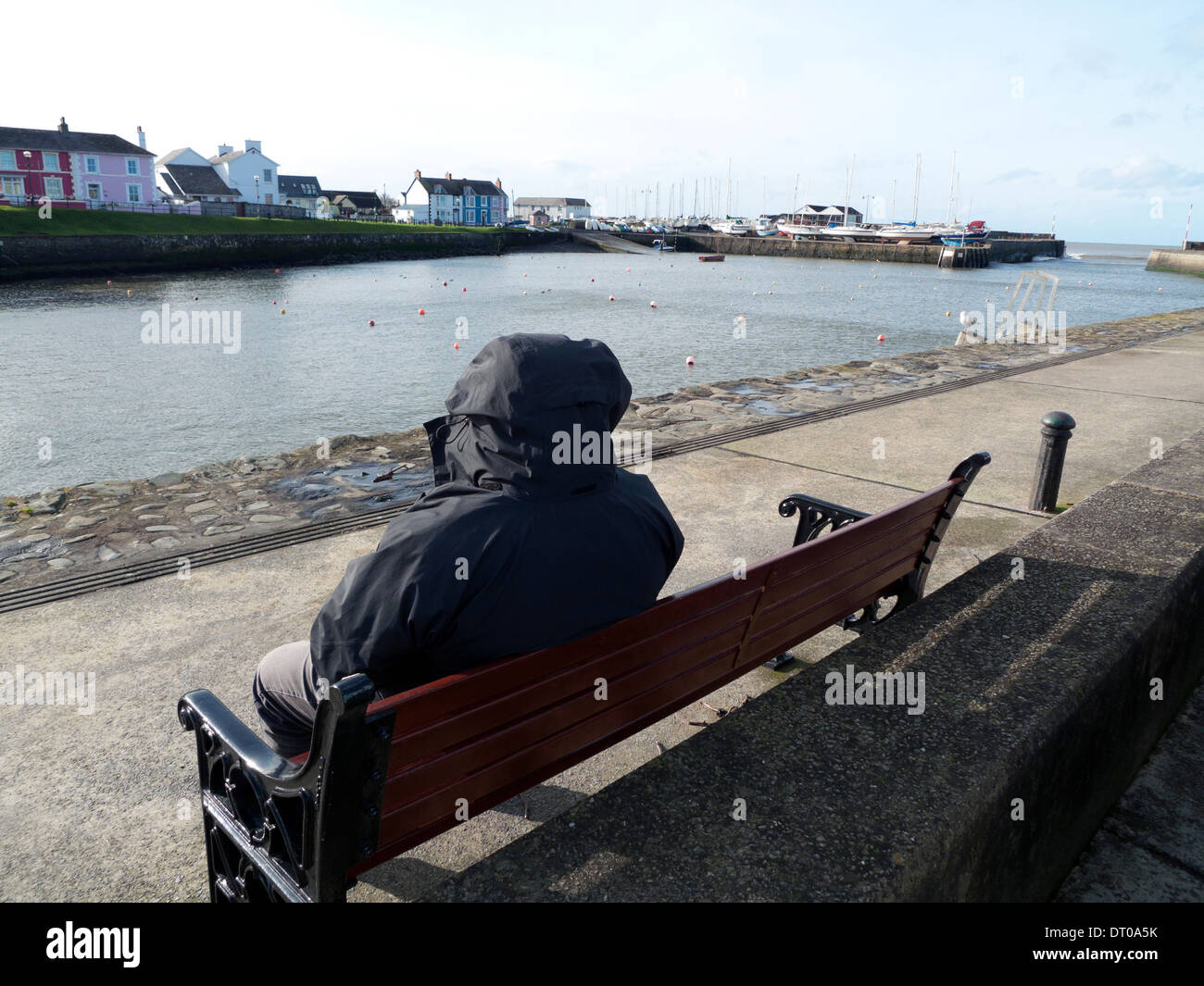 Man in anorak sitting on a bench at Aberaeron harbour Ceredigion Wales UKKATHY DEWITT Stock Photo