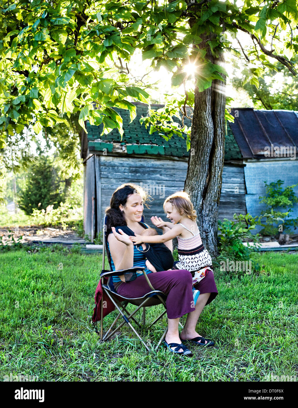 Mother with newborn baby (2-5 months) and daughter (4-5) playing in back yard Stock Photo