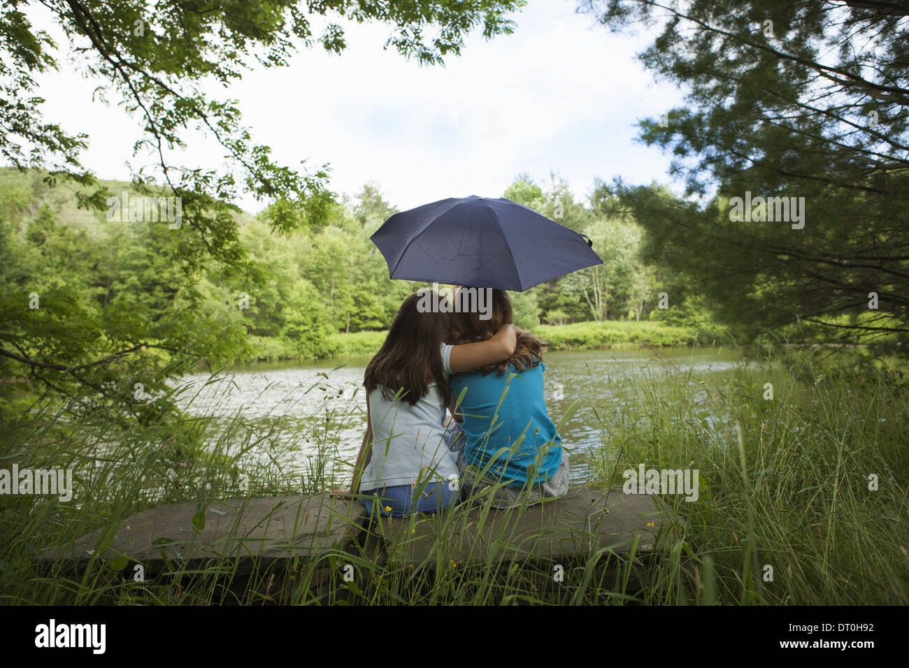 New York state USA Two children girls sitting together by lake Stock Photo