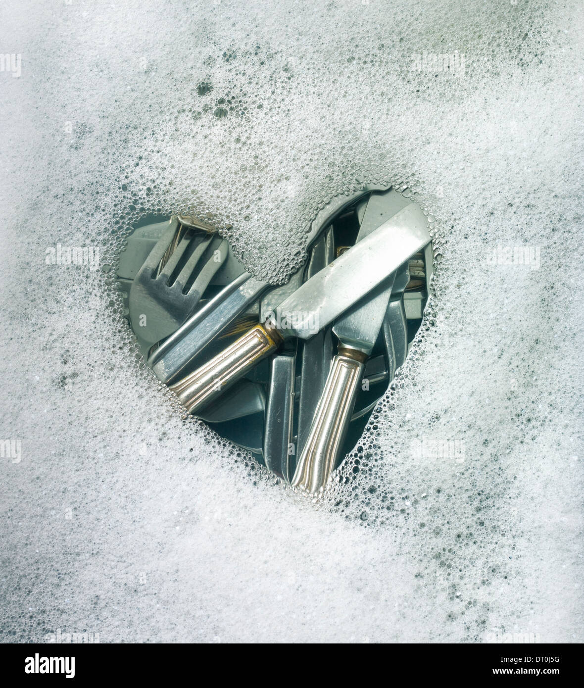 Heart shape in soap suds with cutlery beneath water. Stock Photo