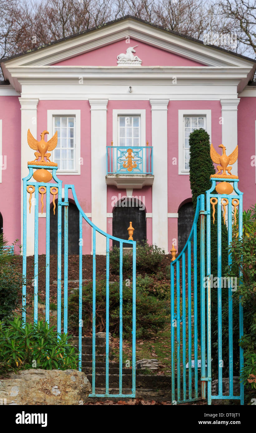 Two metal gates with one open the other closed in front of pink Unicorn House in Italian style holiday village of Portmeirion UK Stock Photo