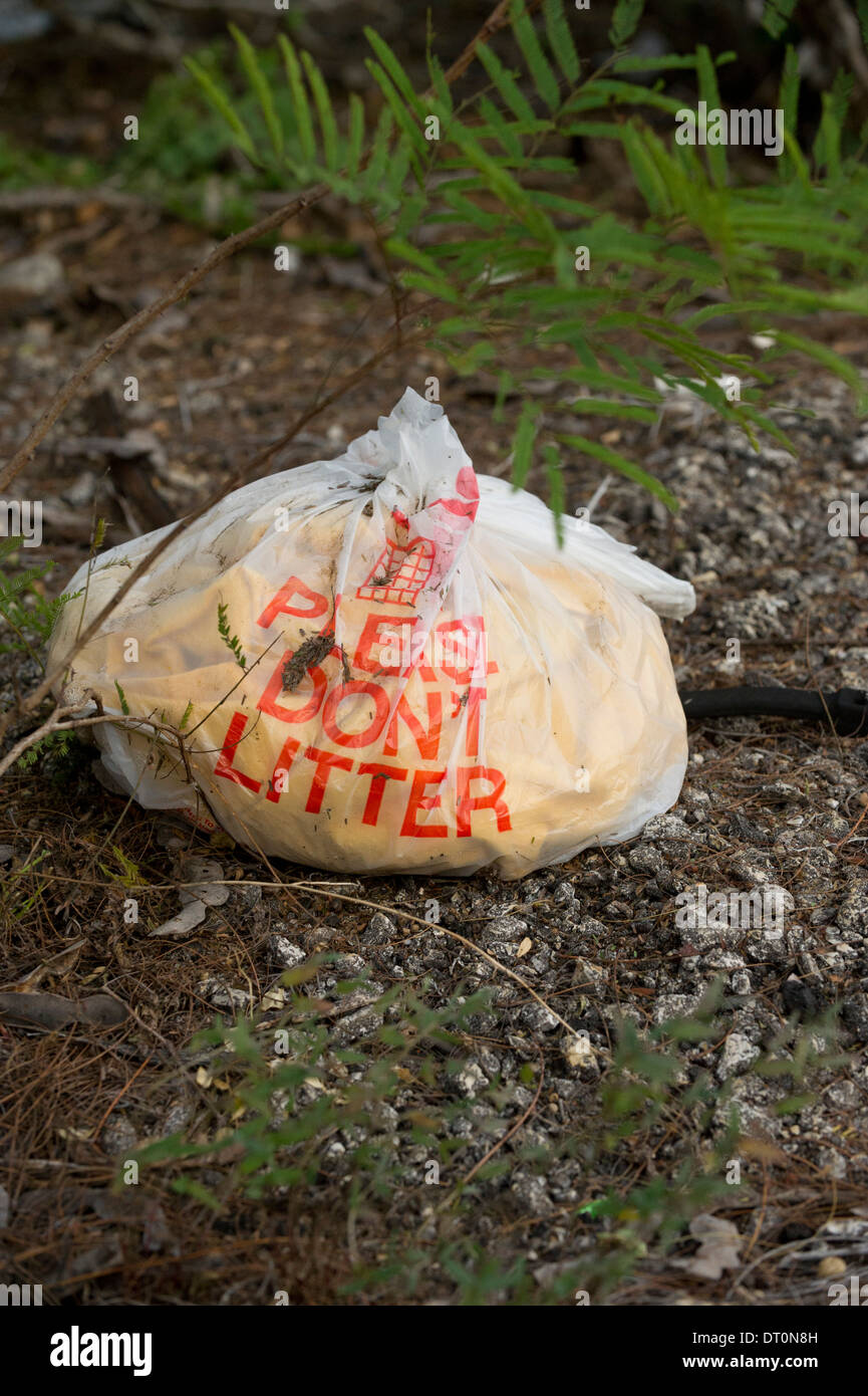 'Please don't litter' plastic bag filled with trash on ground at a rest stop in rural south Texas. Stock Photo