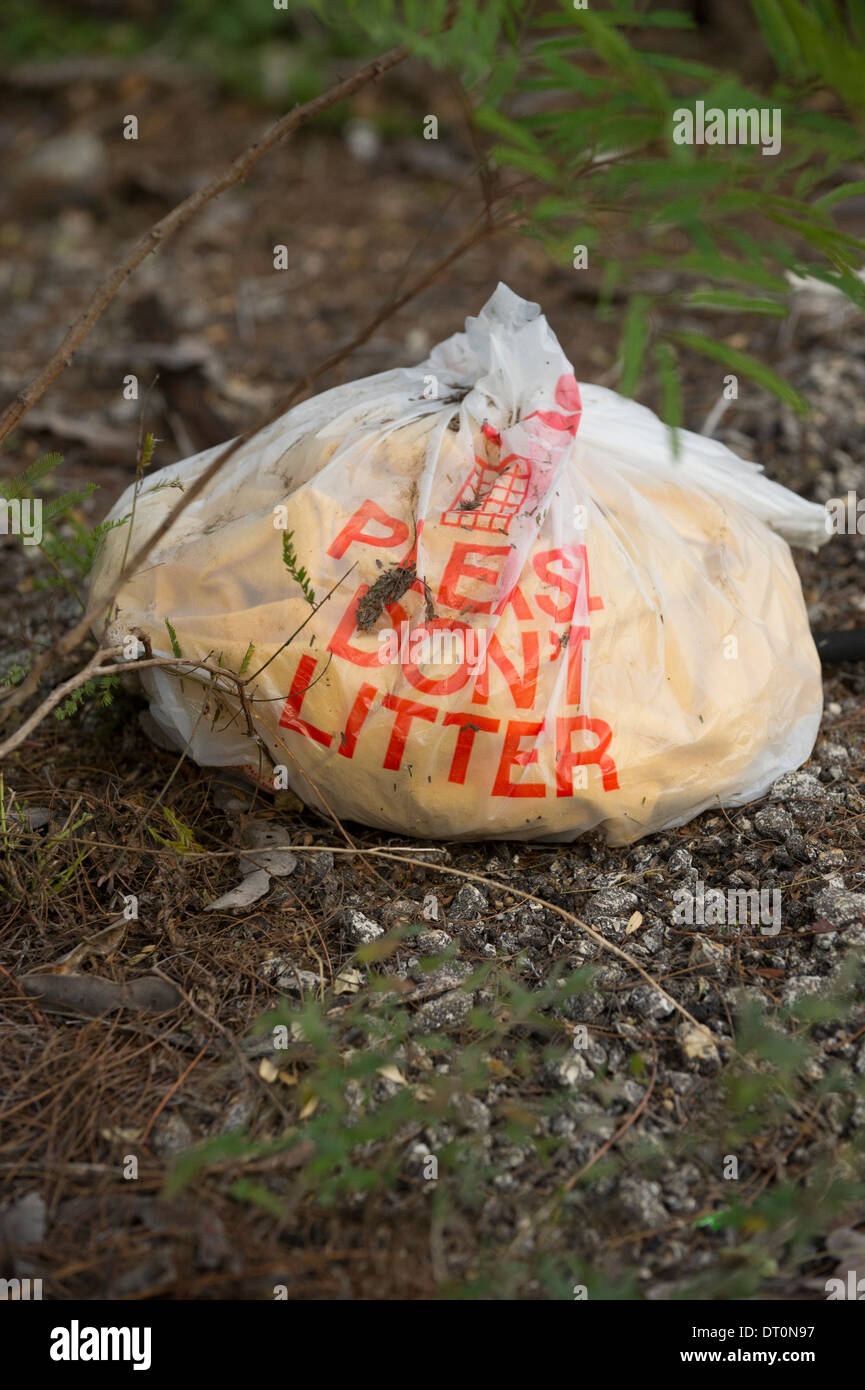'Please don't litter' plastic bag filled with trash on ground at a rest stop in rural south Texas. Stock Photo