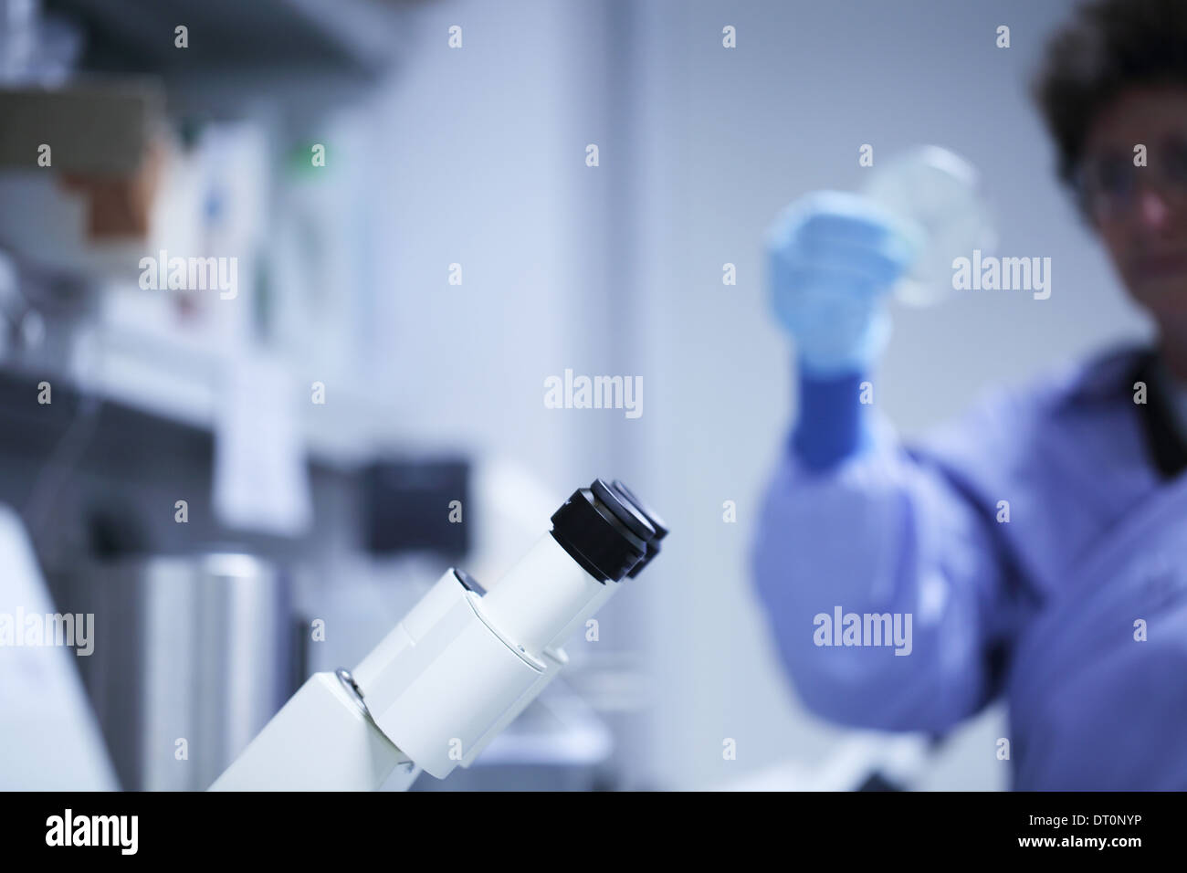 ocular of a microscope and a scientist with blue lab coat Caucasian woman working Stock Photo