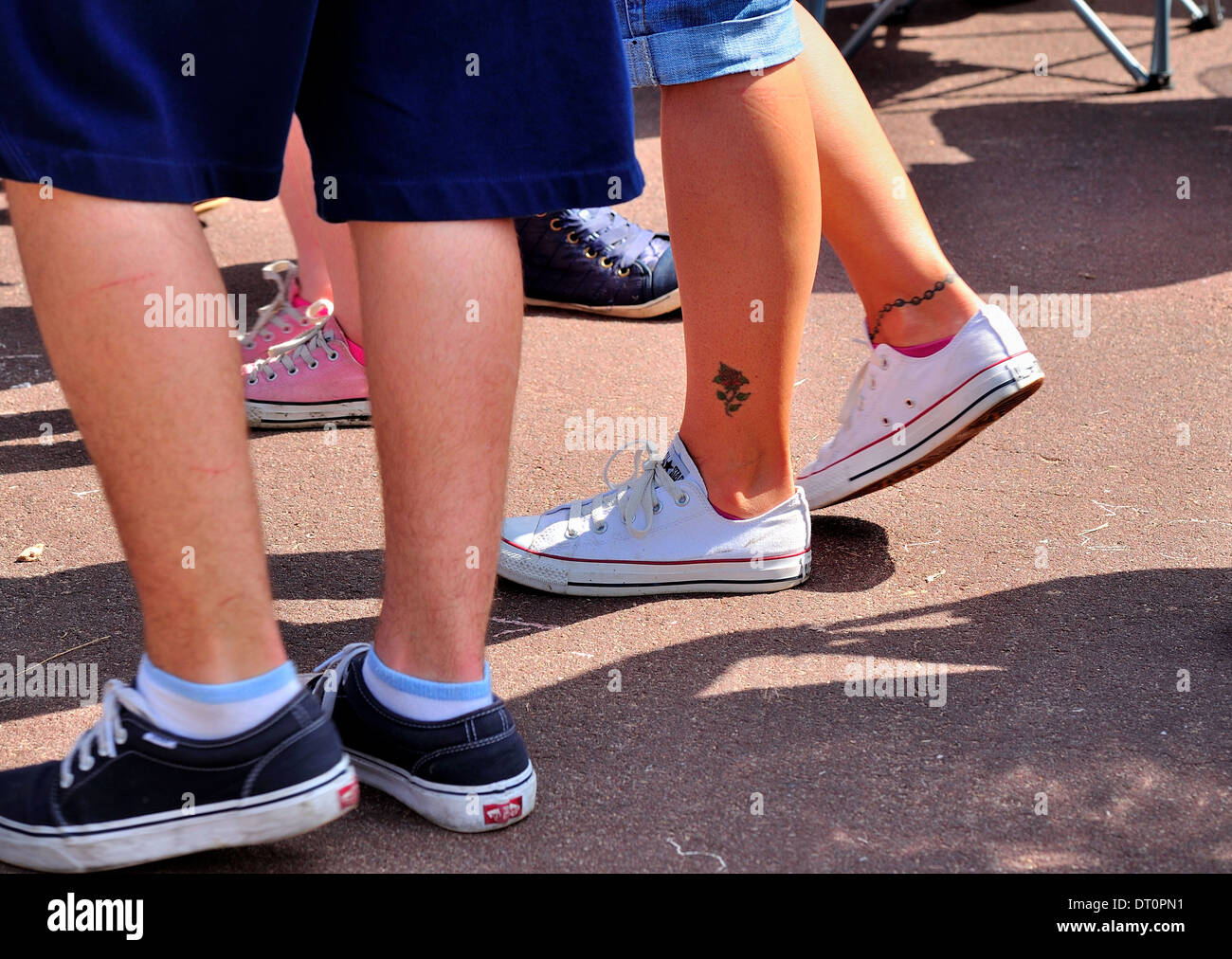 Legs walking on the promenade in summer shorts and trainers with chain and rose ankle tattoos.Clacton Essex UK Stock Photo