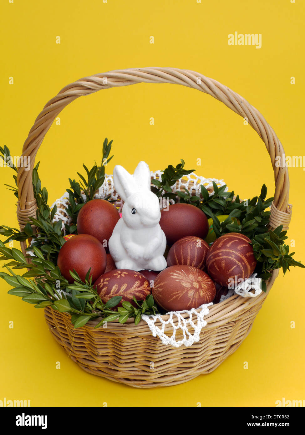 Wicker basket with easter eggs and white plush Easter bunny on yellow background Stock Photo