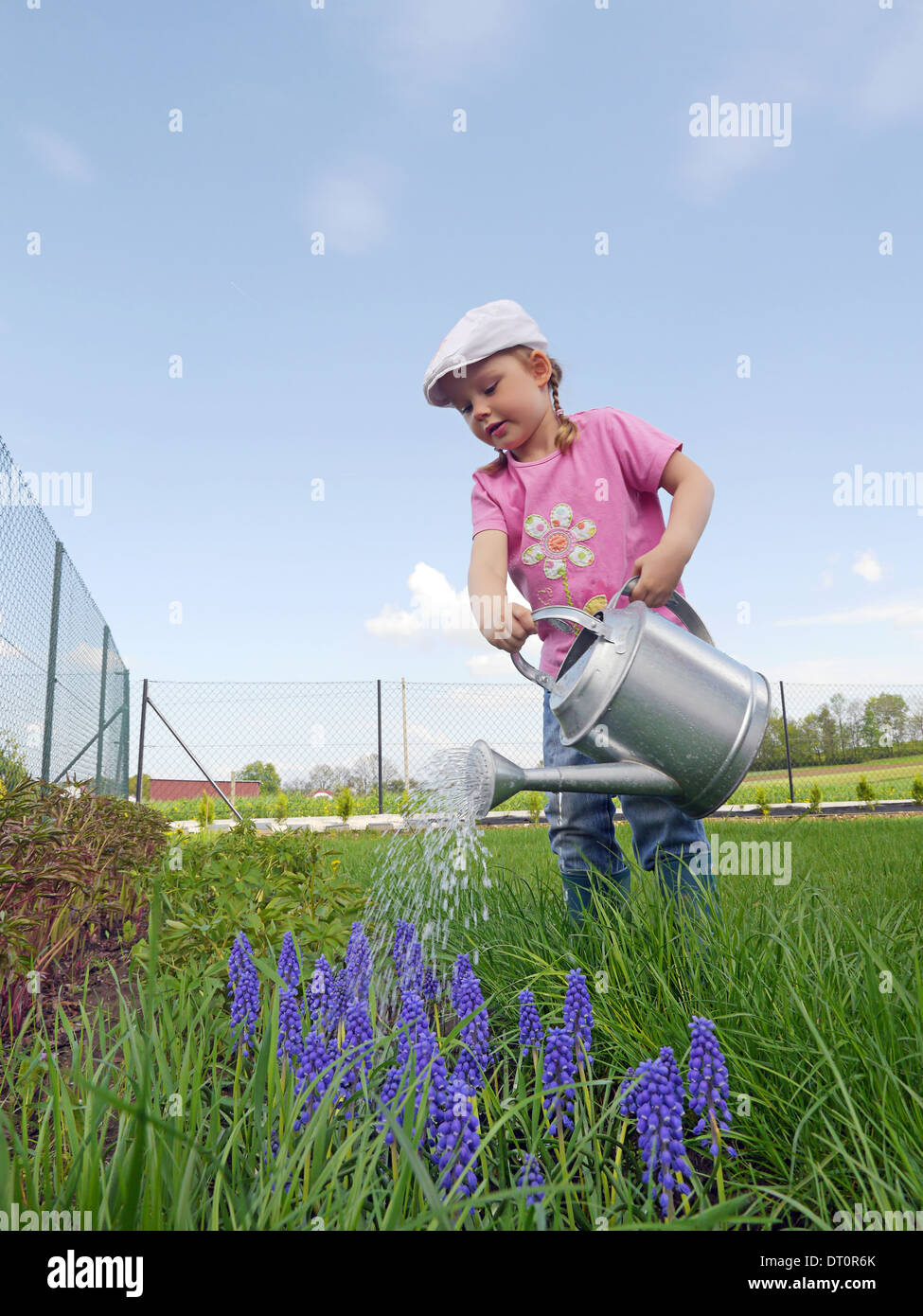 Cute little girl watering flowers growing in the backyard garden Stock Photo