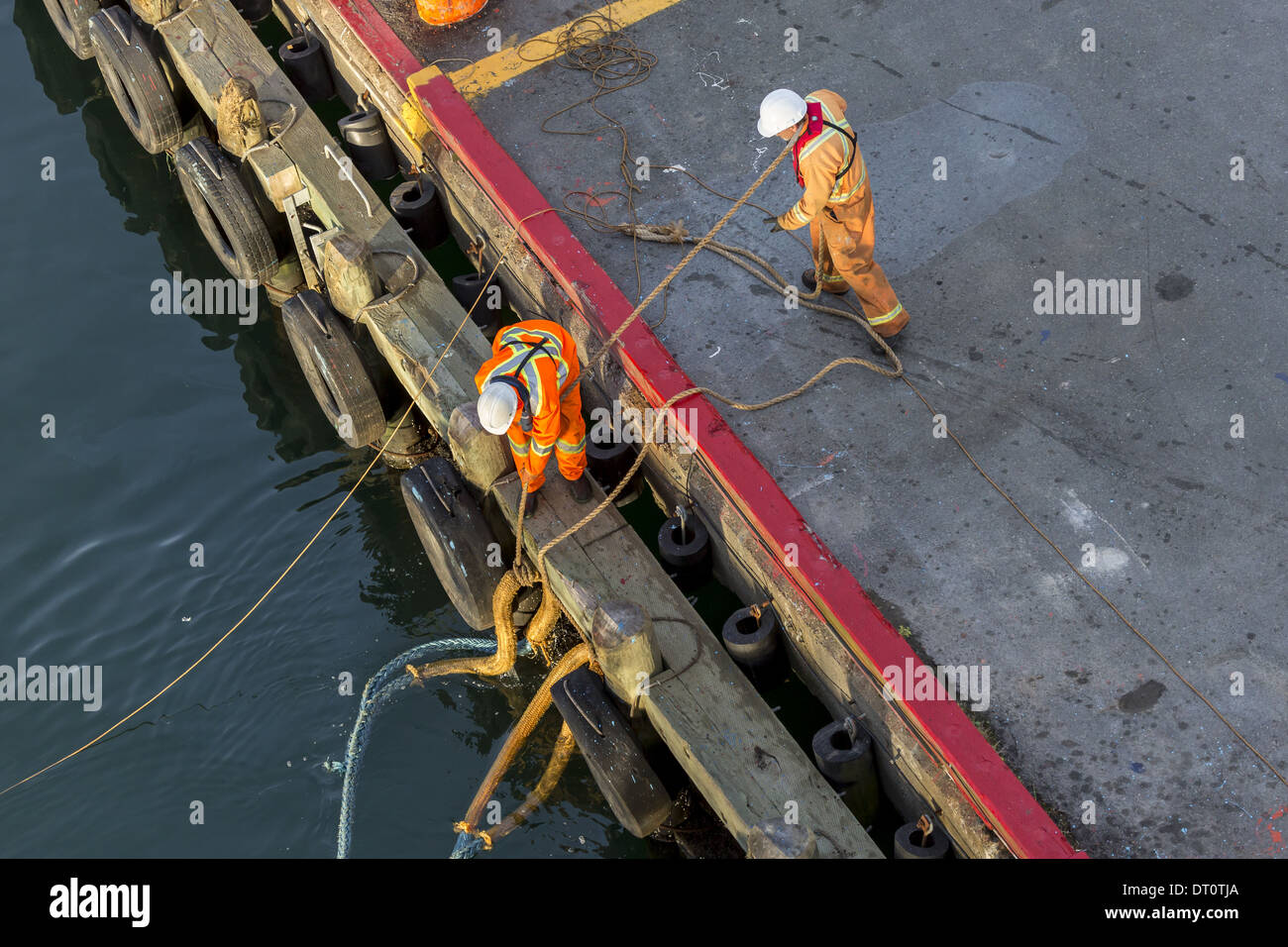 Men securing ships' hawser ropes to bollards on dockside Stock Photo